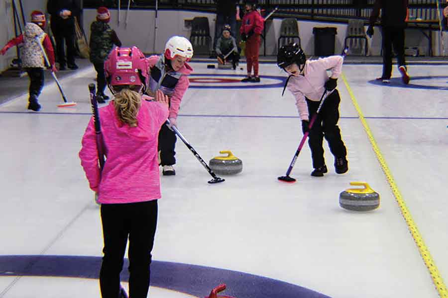 Ava Waluk (front), skip of Team Curl Power, delivers a shot while Sophie Grimes and Aubrey Grondin sweep during the draw-to-the-button competition
