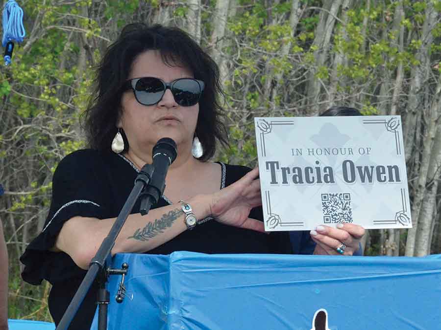 Principal Wendy McPherson speaking about Tracia Owen. The QR code McPherson holds links to resources to prevent childhood sexual exploitation