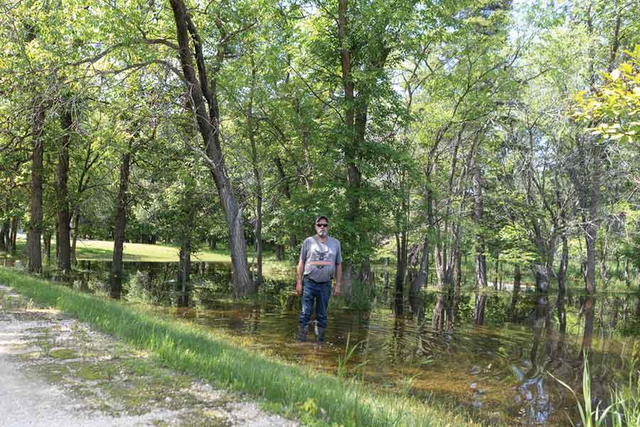 Trevor Sinclair stands in the flooded front yard of his Winfield Road property, where standing water remains more than three weeks after the historic June 9-10 rainfall. Sinclair says ongoing drainage issues have left his family unable to fully access or restore their property